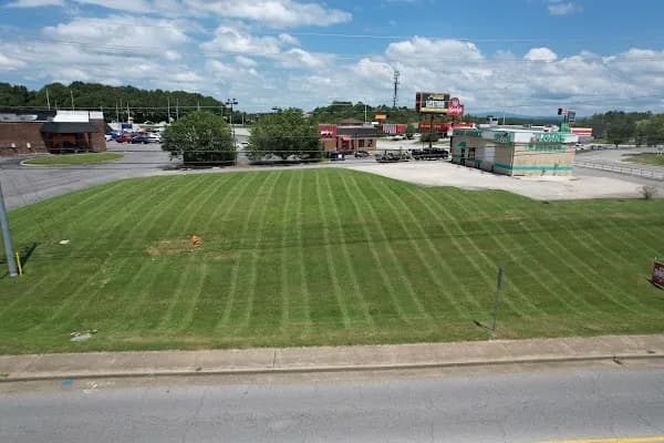 Large open lot mowed in even stripes beside a commercial strip