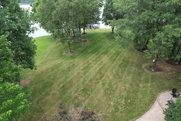 Mowed lawn running down toward the water under mature shade trees